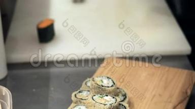 制作和切割橙色寿司卷的过程。 男人用竹垫卷起寿司。 准备好的寿司卷